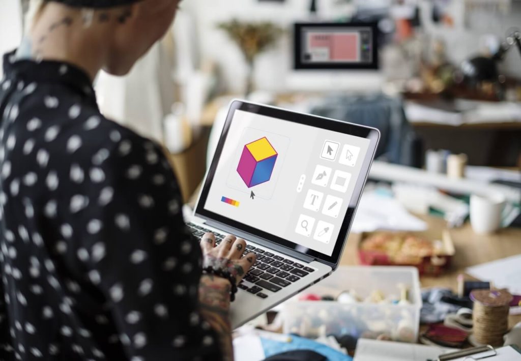 A graphic designer working on a laptop to illustrate a cube